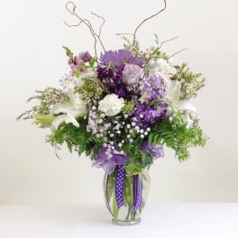 Purple and white floral arrangement in a clear glass vase with ribbon