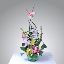 Tall floral arrangement in a green glass vase with pink lilies and pastel blooms