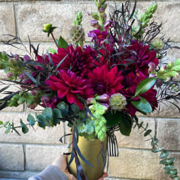 Magenta dahlias in a gold vase with dark foliage and green accents