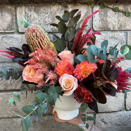 Bouquet of peach roses, coral dahlias, and pink-red blooms in a white vase