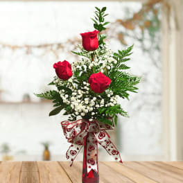 Red roses in a tall glass vase with baby's breath and a heart-patterned ribbon