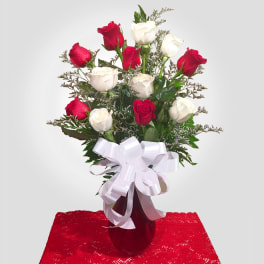 Red and white roses in a red vase with a white ribbon bow