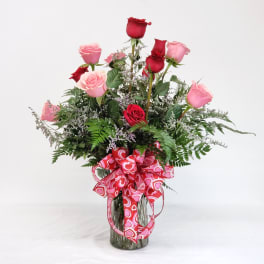 Bouquet of pink and red roses in a glass vase with a heart ribbon