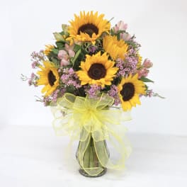 Bouquet of sunflowers and pink filler flowers in a glass vase with yellow ribbon
