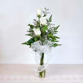 White roses in a clear glass vase with a white ribbon bow