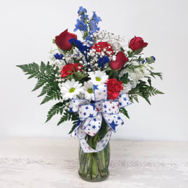 Bouquet of red roses, white daisies, and blue flowers in a glass vase with a star ribbon