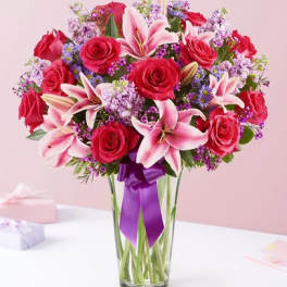 Bouquet of red roses and pink lilies in a clear glass vase with a purple ribbon