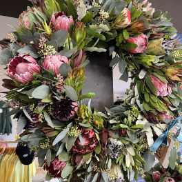 Large wreath of pink protea and eucalyptus on a dark stand