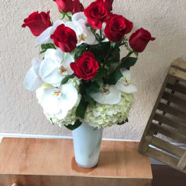 Red roses and white orchids arranged in a tall white vase