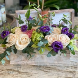Cream roses and purple blooms arranged in a low wooden box