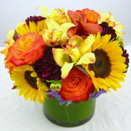 Bouquet of sunflowers, orange roses, and yellow calla lilies in a green vase