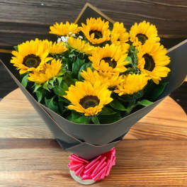 Bouquet of yellow sunflowers wrapped in black paper with a pink ribbon