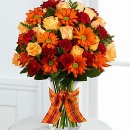 Bouquet of orange daisies and red and peach roses in a glass vase