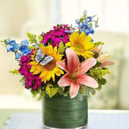 Colorful bouquet with sunflowers, lilies, and blue flowers in a glass vase