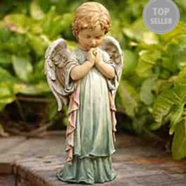 Small praying angel figurine in a garden setting