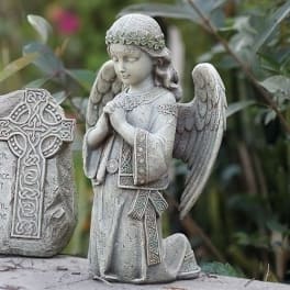 Stone angel statue kneeling beside a Celtic cross marker