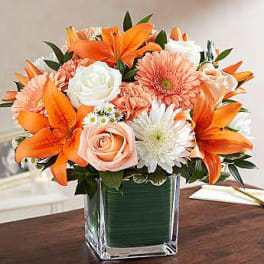 Orange lilies and peach roses in a clear square vase