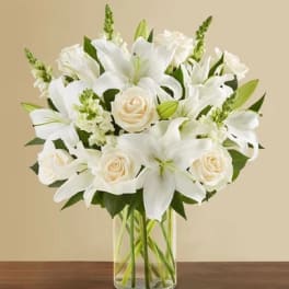 White lilies and cream roses arranged in a clear glass vase