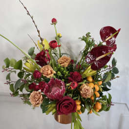 Mixed floral arrangement with red roses, burgundy anthuriums, and orange berries in a copper vase
