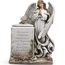Angel statue beside a memorial stone with small pink roses