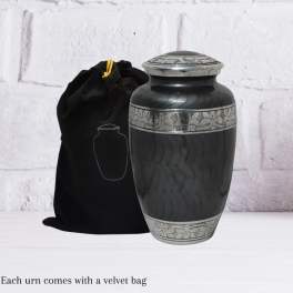 Black memorial urn with silver detailing beside a velvet bag