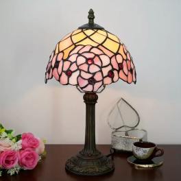 Stained-glass table lamp with pink and yellow shade beside a small rose bouquet