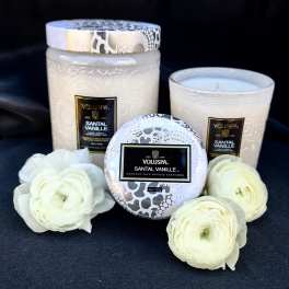 Three white candles with patterned lids and white ranunculus blooms.