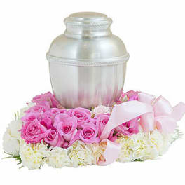 Pink roses arranged around a silver urn with a pink ribbon