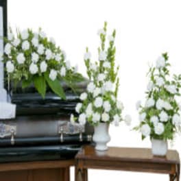 White floral funeral arrangements in white vases beside a casket
