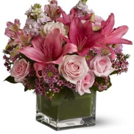 Pink lilies and roses arranged in a clear square vase