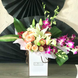 Bouquet of peach roses, white lilies, and purple orchids in a white gift box