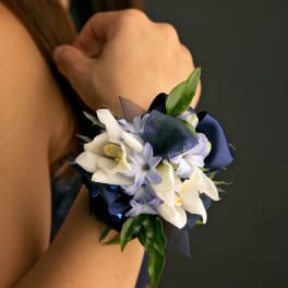 Wrist corsage with white and pale blue flowers and navy ribbon on a person’s arm