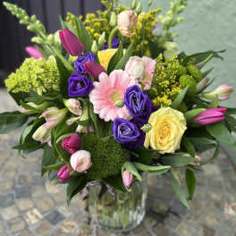 Vase arrangement of pink tulips, purple lisianthus, a yellow rose and mixed blooms in a clear glass vase.