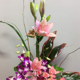 Tall floral arrangement with pink lilies, purple orchids, and roses in a black vase