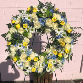 Wreath of white roses, blue flowers, and yellow duck decorations on a stand