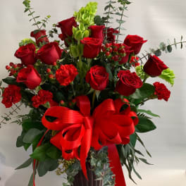 Red roses and carnations in a red glass vase with a large red bow