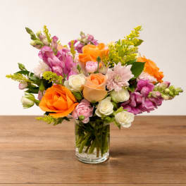 Mixed bouquet of orange, pink, and white flowers in a clear glass vase
