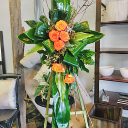 Tall floral standing arrangement with orange roses and glossy tropical leaves