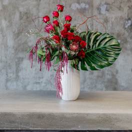 Red rose arrangement in a white vase with tropical leaves