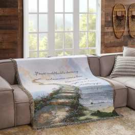 A decorative throw blanket with a seaside staircase scene and cursive text draped over a sofa
