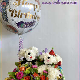 Birthday balloon above a flower arrangement with two white dog faces