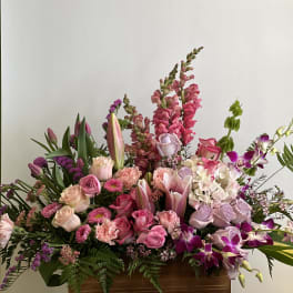 Large mixed bouquet with pink roses, lilies, orchids, and snapdragons in a wooden container