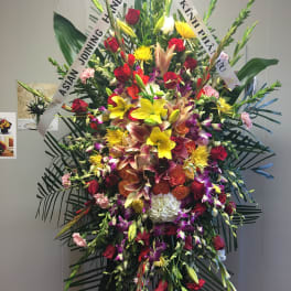 Large standing floral spray with mixed blooms and white condolence ribbons