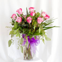 Pink roses in a glass vase with a purple ribbon