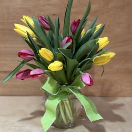 Bouquet of yellow and pink tulips in a glass vase with a green ribbon