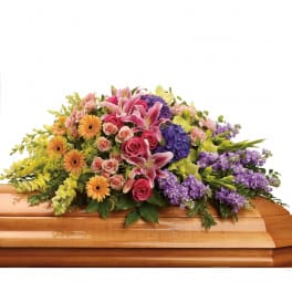 Colorful floral casket spray with lilies, roses, gerberas, and purple blooms
