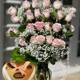 Pink roses in a glass vase with baby's breath and a heart-shaped chocolate box