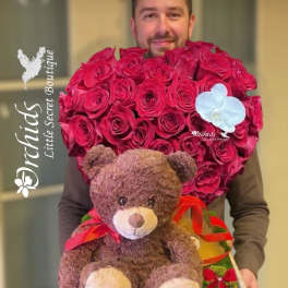 Man holding a heart-shaped rose arrangement with a teddy bear and ribbon