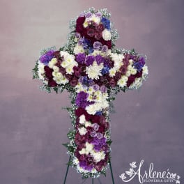 Tall cross-shaped arrangement of white, purple, and burgundy flowers on a metal easel stand
