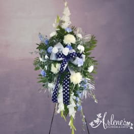 Tall standing spray of white and blue flowers with star-patterned ribbon on an easel stand